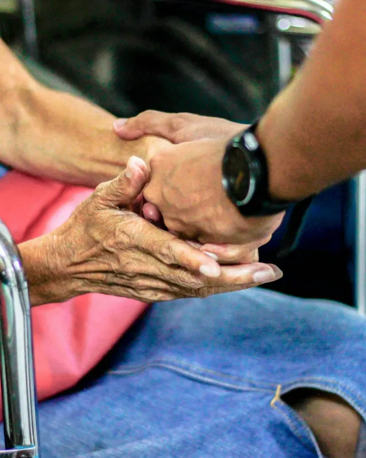 Cuidadora segurando as mãos de uma idosa em cadeira de rodas